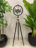 Modern Floor clock with a decorative design on a tripod stand, surrounded by potted plants.