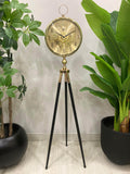 Gold tripod clock with decorative face in a room with plants