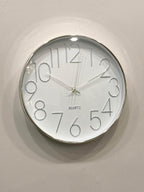 Round wall clock with silver frame and white face on a light gray background