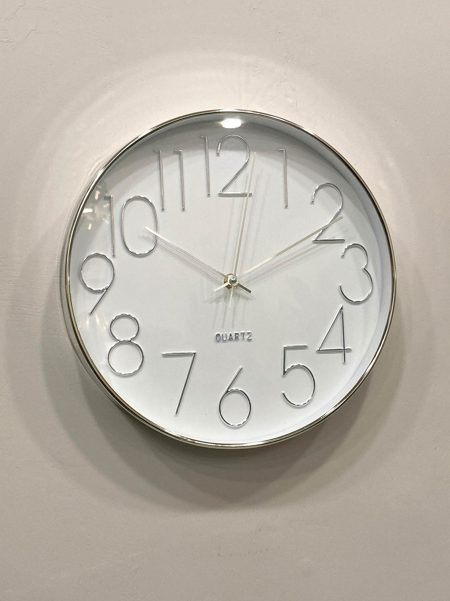 Round wall clock with silver frame and white face on a light gray background