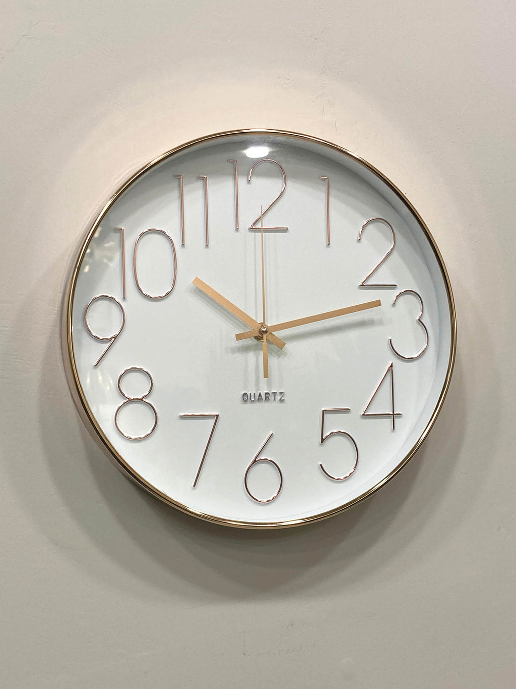 Wall clock with gold frame and white face on a light gray wall