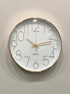 Wall clock with gold frame and white face on a light gray wall