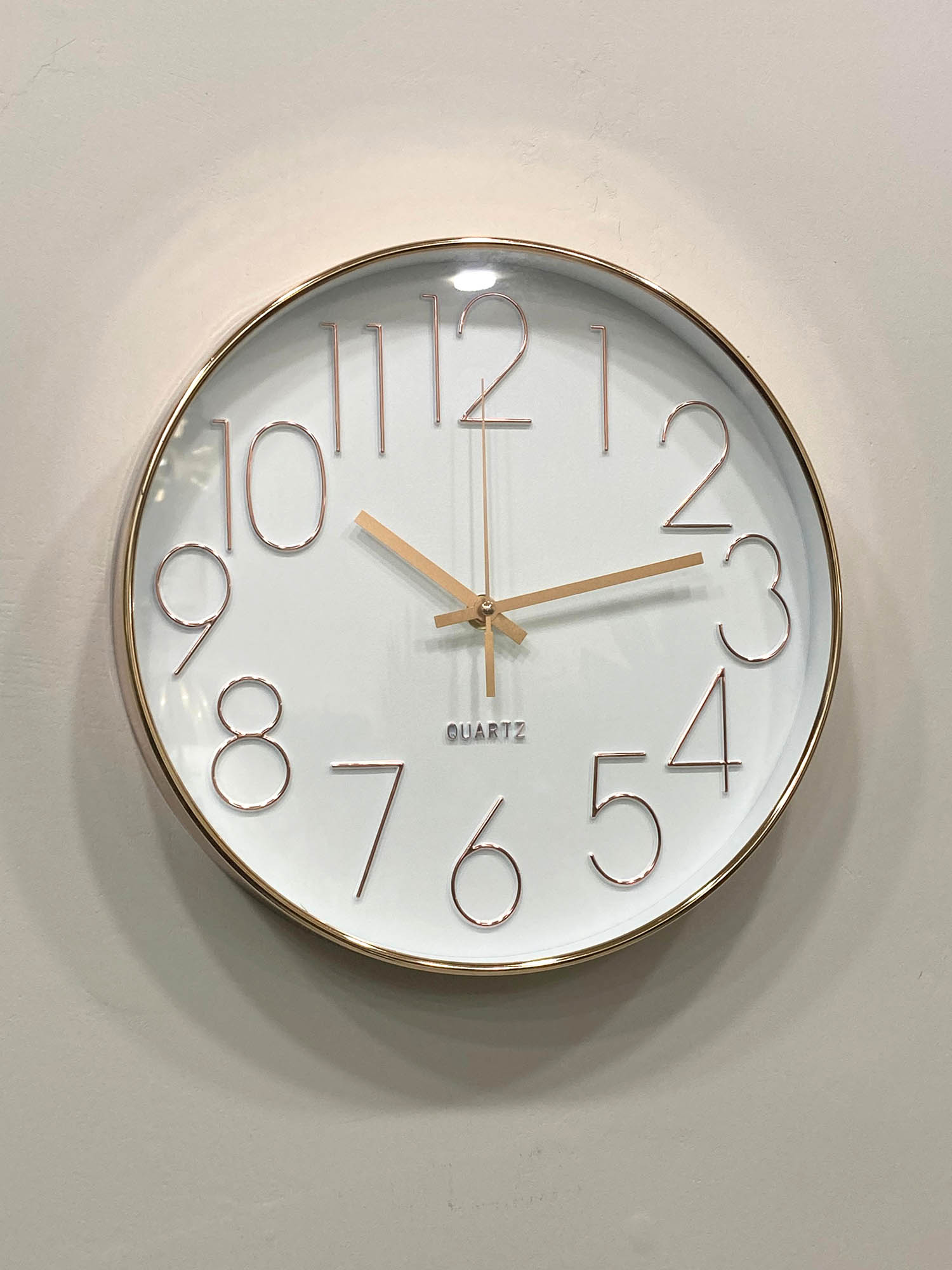 Wall clock with gold frame and white face on a light gray wall