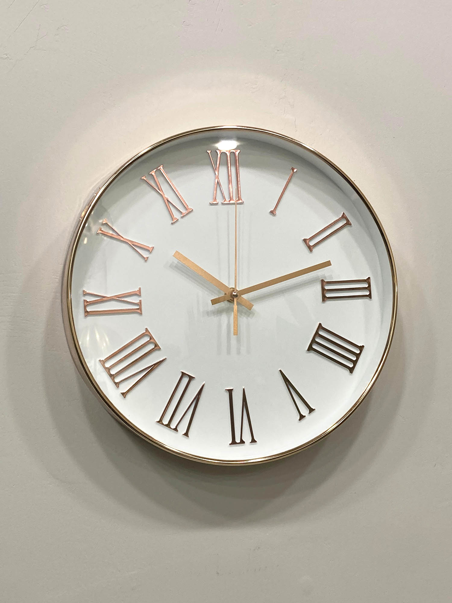 Round wall clock with gold hands and Roman numerals on a light gray background