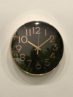 Modern wall clock for living room décor 
Wall clock with black face and gold numbers and hands on a light background