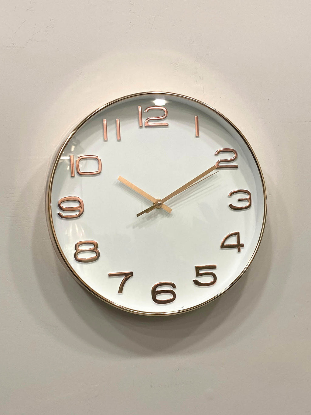 Round wall clock with rose gold frame and numbers on a light gray background