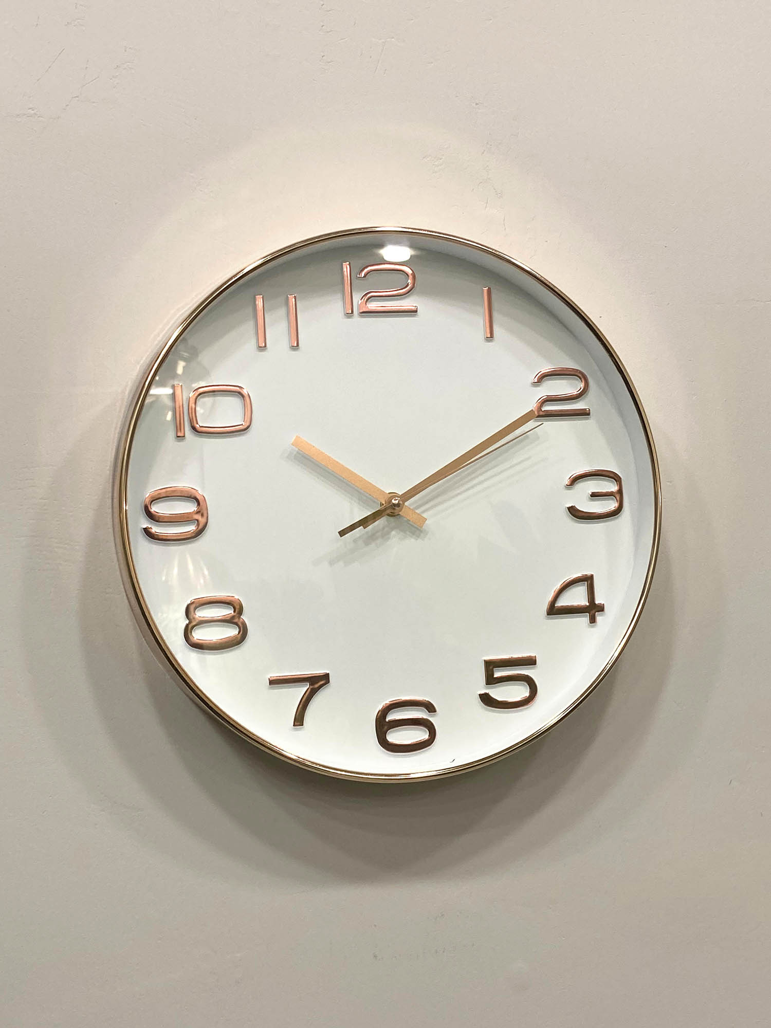 Round wall clock with rose gold frame and numbers on a light gray background