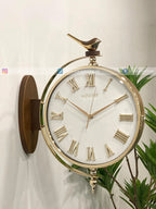 Gold Modern wall clock for living room décor with Roman numerals on a white wall with green plants.