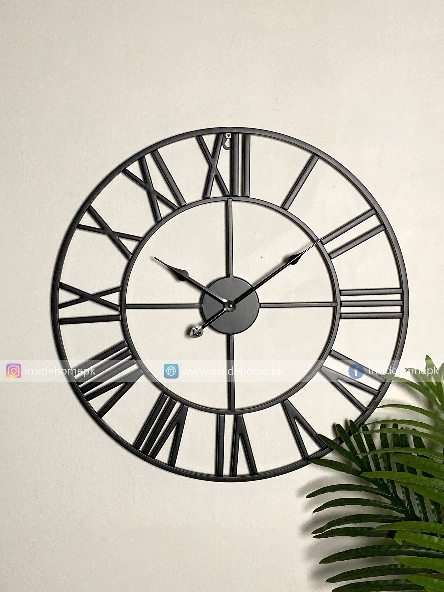Large black Modern wall clock for living room décor with Roman numerals on a light beige wall.