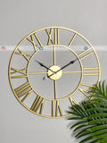 Gold Modern wall clock for living room décor with Roman numerals on a gray wall with a plant in the corner.