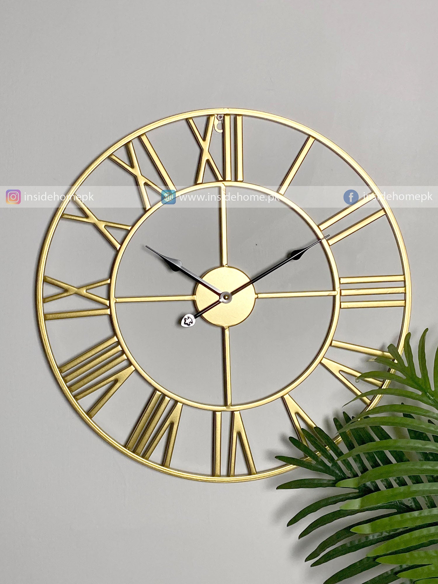 Gold Modern wall clock for living room décor with Roman numerals on a gray wall with a plant in the corner.