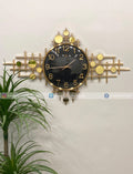 Decorative Modern wall clock for living room décor with gold and black design on a white wall with a plant on the left.