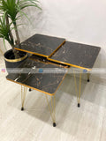 Set of three black marble-style tables with gold legs on a light wooden floor.