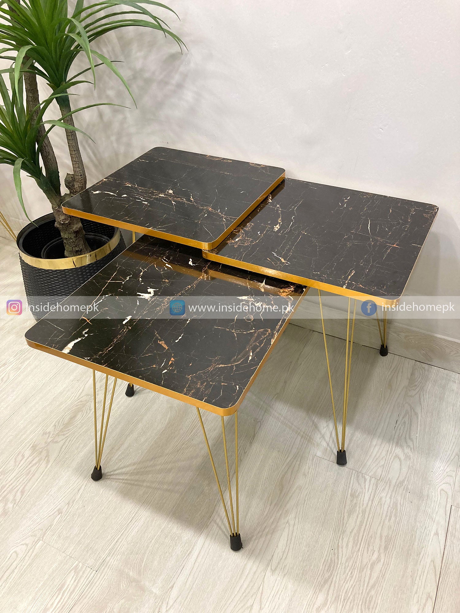 Set of three black marble-style tables with gold legs on a light wooden floor.