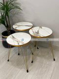Three marble-top side tables with gold metal legs on a light wooden floor.