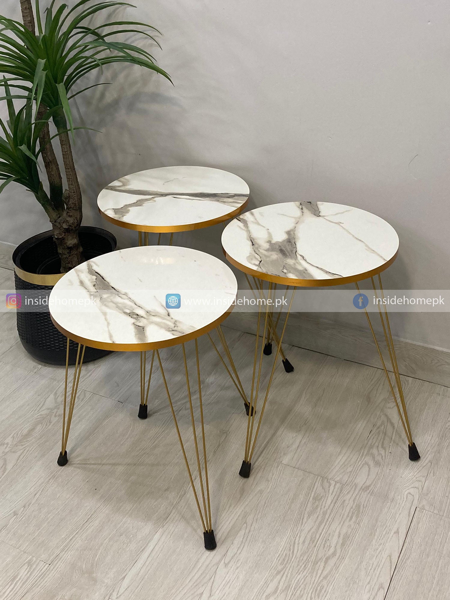 Three marble-top side tables with gold metal legs on a light wooden floor.